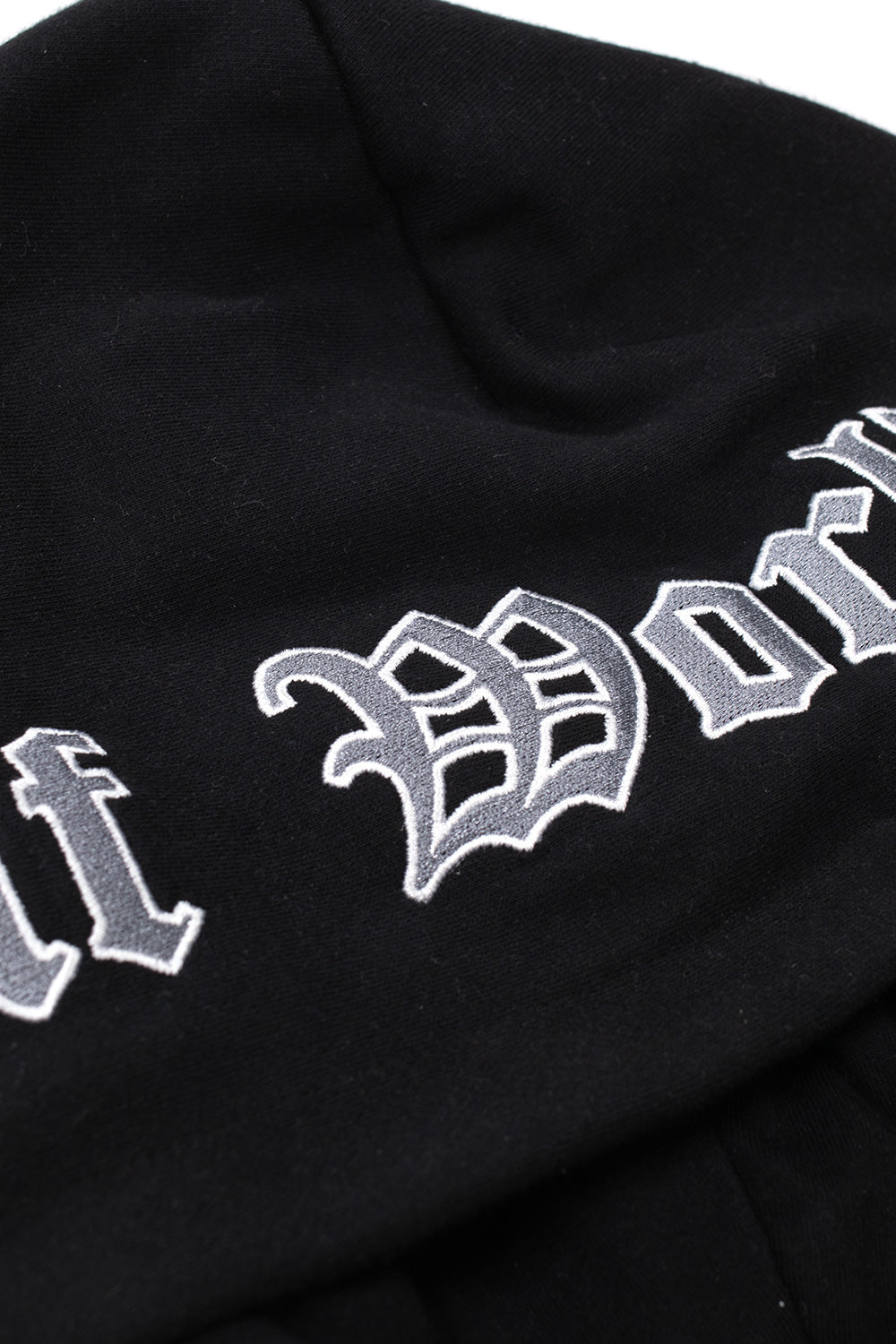 Close-up detail shot of the black fleece hood on the HUF Olympia Camo overshirt, highlighting the thick silver-grey and white embroidered Gothic Old English typography stitching spelling Huf Worldwide across the brushed fleece rim.