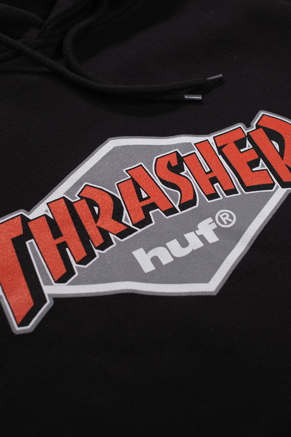 Black HUF Thrasher capsule hoodie featuring retro-inspired printed logos, kangaroo pocket, and soft cotton-poly construction.