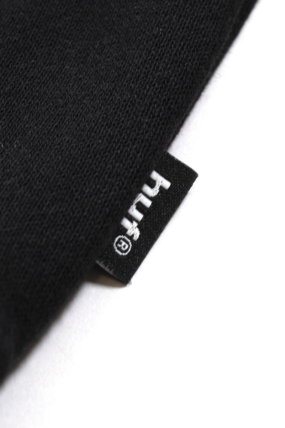 Macro image of the HUF Worldwide woven logo label on a black cotton blend hoodie, emphasizing quality streetwear construction