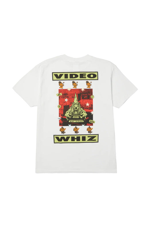 Back flat lay view of the white HUF Video Genie T-Shirt, crafted from 250g 100% cotton, featuring a large multicolor graphic framed by bold black "VIDEO" and "WHIZ" typography, displaying a central wizard holding a VHS tape on a red halftone background, surrounded by yellow cartoon genies and holographic silver stars