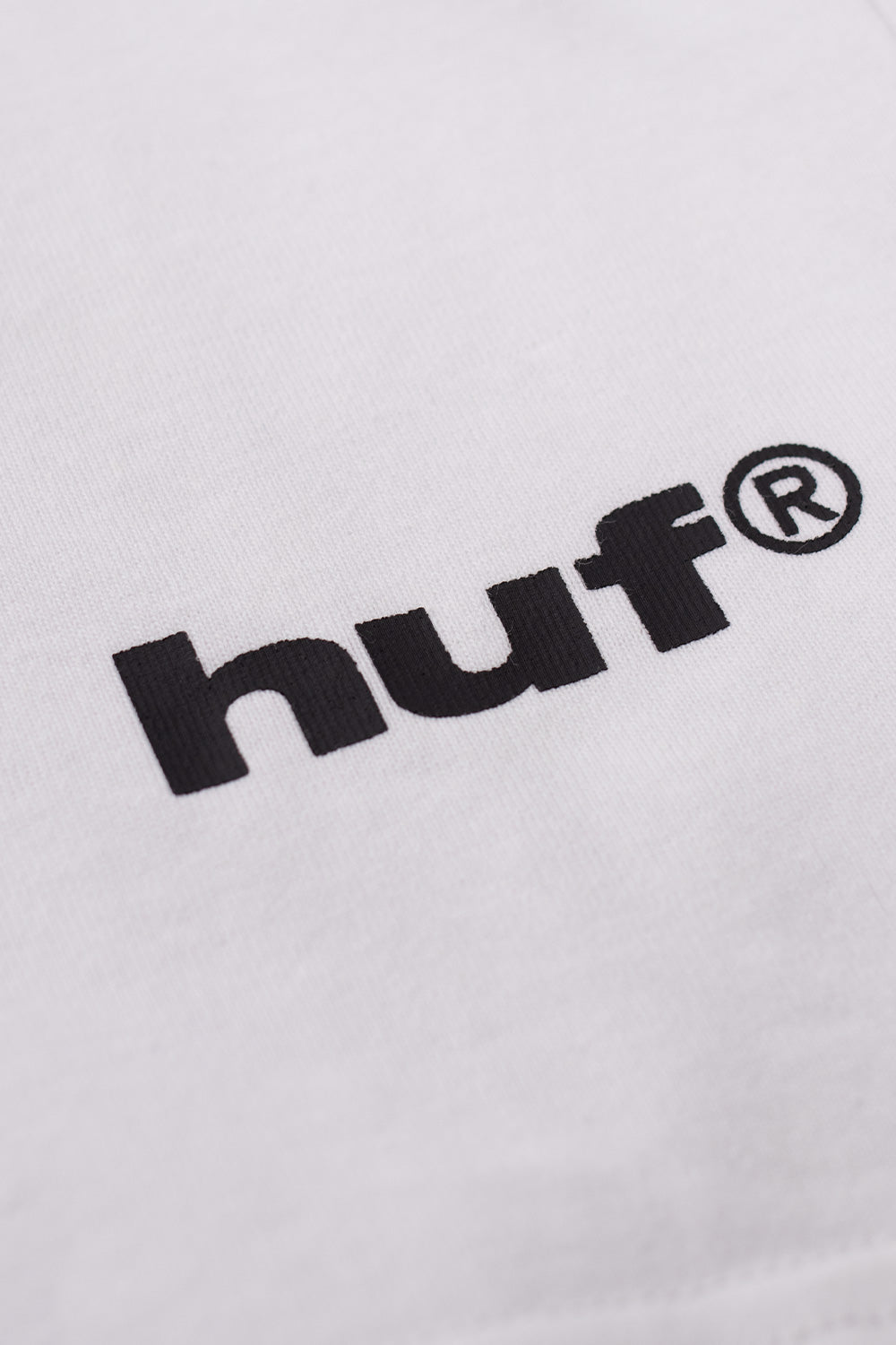 Detail shot of black HUF logo print on white HUF x Metal Gear Solid Battlefield T-shirt made in Mexico from premium cotton fabric