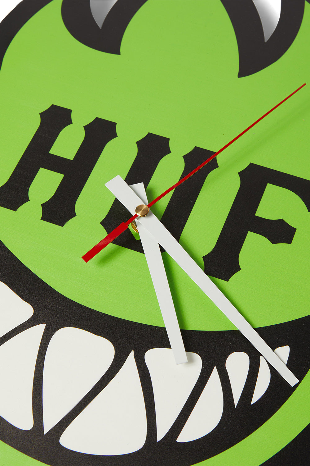 Detailed close-up shot of the clock hands on the HUF X Spitfire Bighead wall clock, showing the gold center pin holding white hour and minute hands and a red second hand against the bright green acrylic flame design.