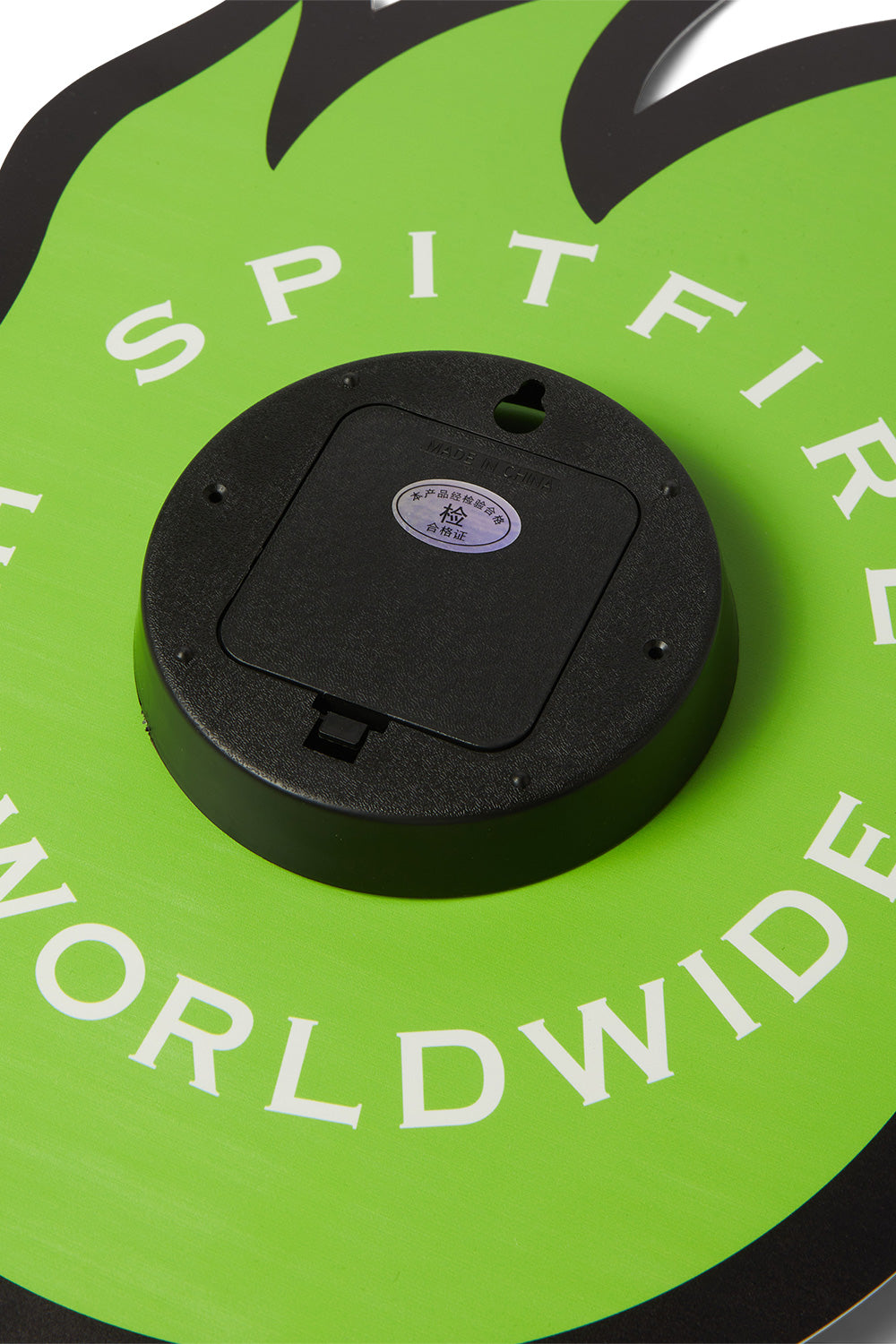 Close-up view of the back mechanism on the HUF X Spitfire Bighead acrylic clock, showing the battery compartment door, wall hanging mounting notch, and white printed SPITFIRE HUF WORLDWIDE branding.