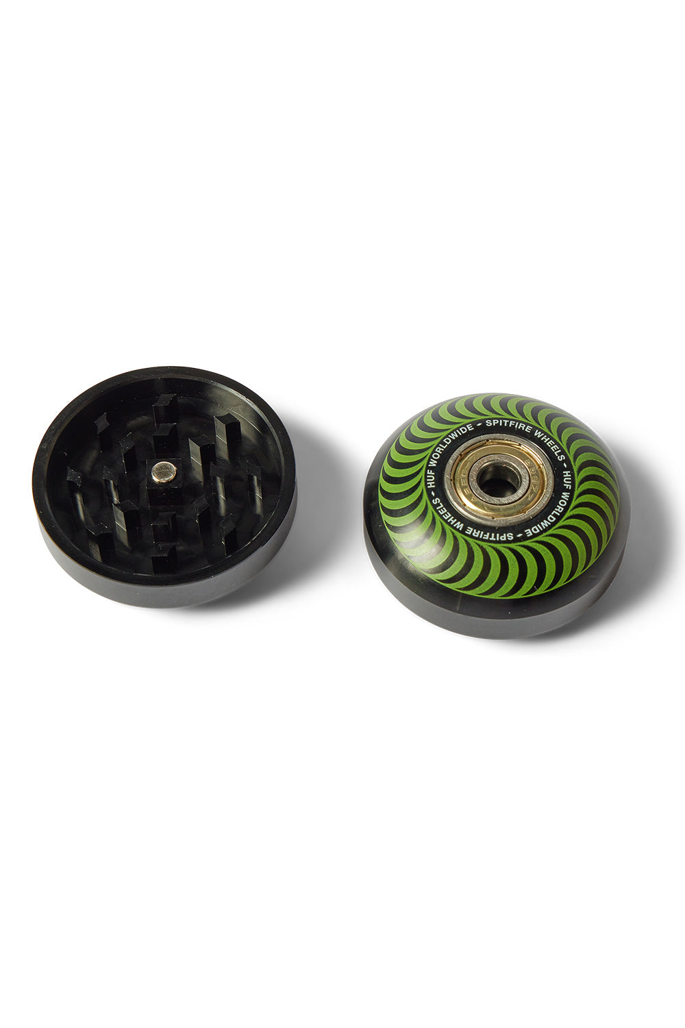 Overhead shot showing the top lid removed from the HUF X Spitfire skateboard wheel grinder, displaying the interior black diamond-shaped grinding teeth and magnetic closure next to the green swirl wheel top section.