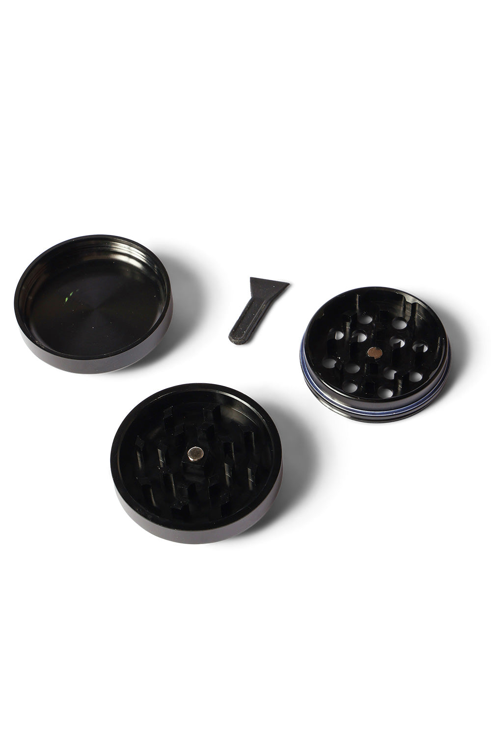 All three disassembled pieces of the HUF X Spitfire Classic 3-piece herb grinder laid out, showing the top magnetic lid, middle sifter section with grinding teeth and drop holes, bottom collection chamber, and a small black scraper tool.