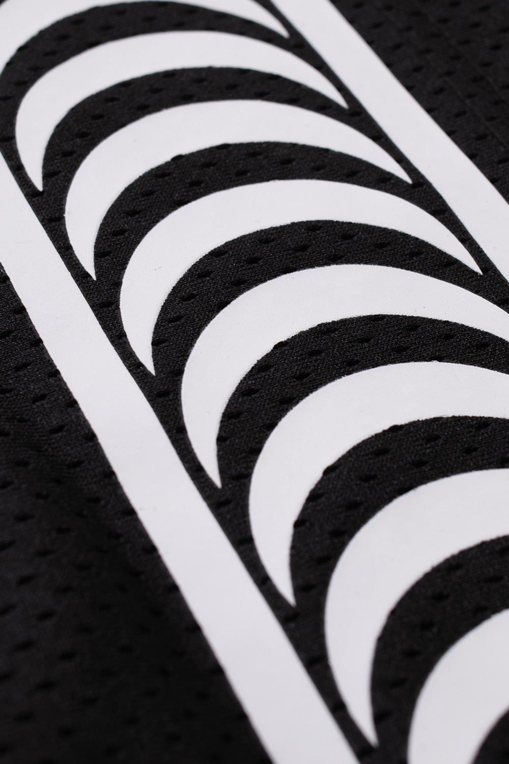Macro detail shot of the sleeve arm stripe on the black HUF X Spitfire jersey, showing the bold white curved Spitfire Classic Swirl repeating pattern screen-printed over the breathable perforated black polyester mesh jersey fabric.
