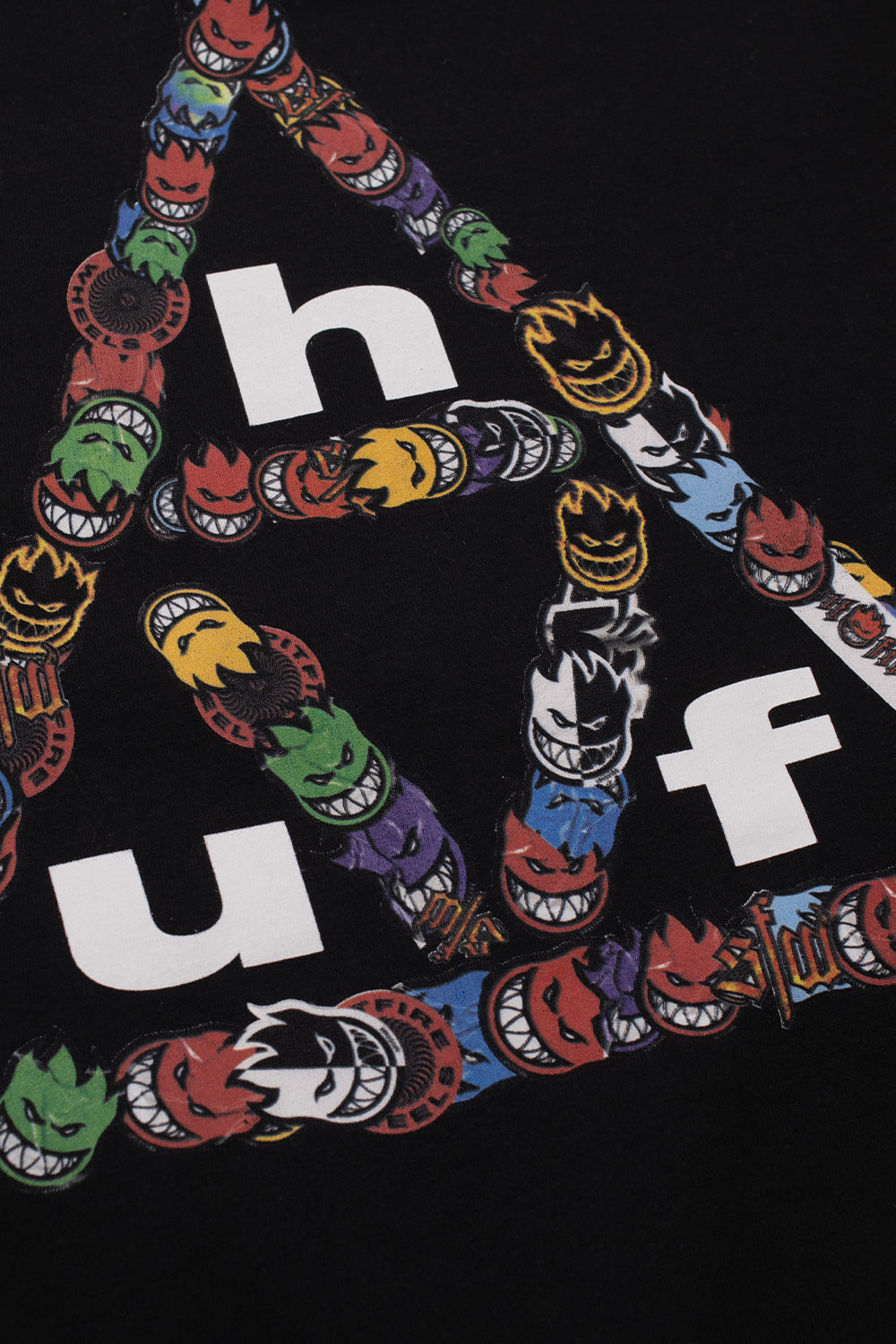 Close-up detail shot of the backprint graphic on the black HUF X Spitfire tee, highlighting the intricate multi-colored Spitfire Bighead flame stickers outlining the white HUF letter logo.