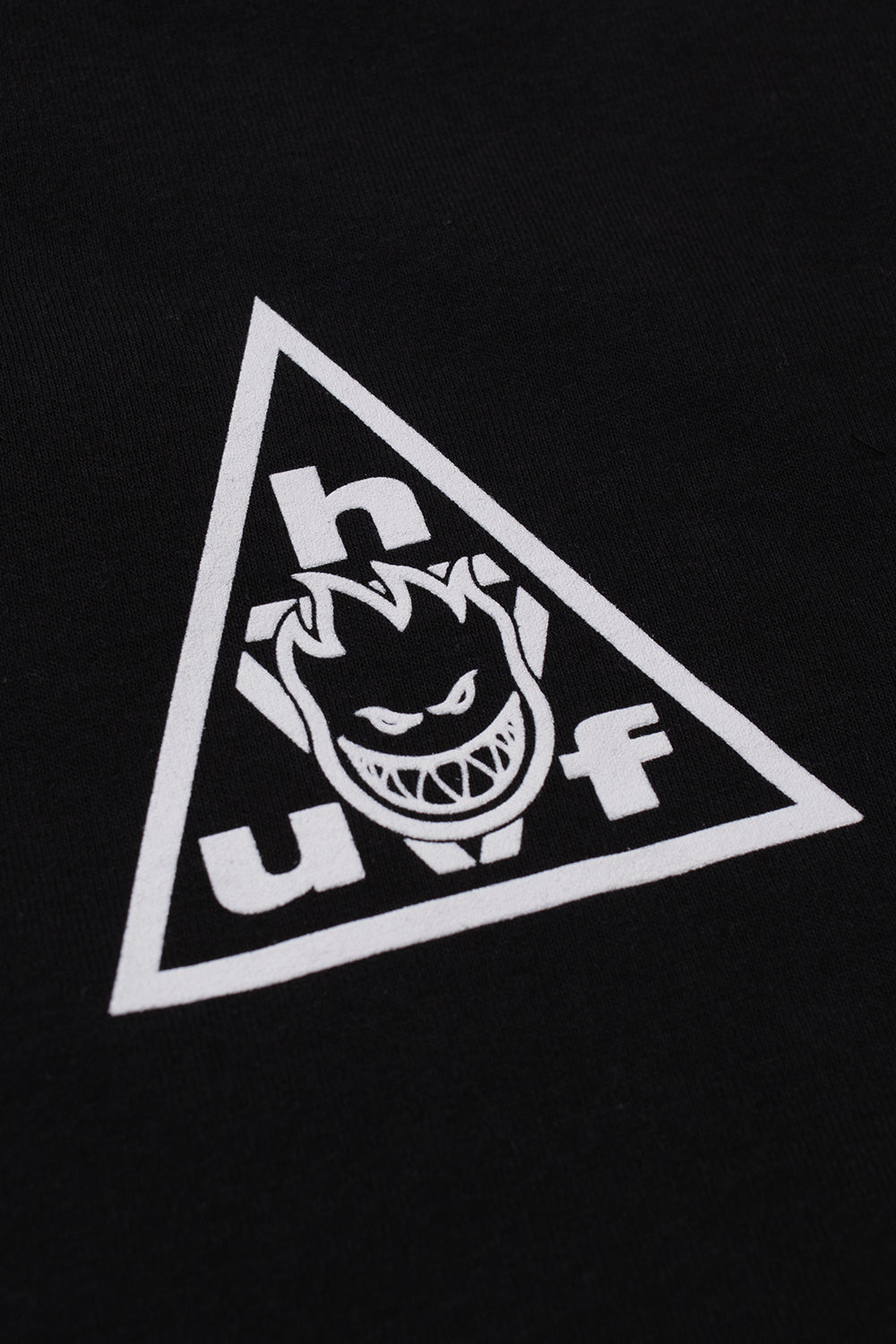 Macro detail shot of the white screen-printed chest graphic on the black HUF X Spitfire Sticker T-Shirt, showing the clean print quality of the classic Triple Triangle frame housing the grinning Bighead flame character.