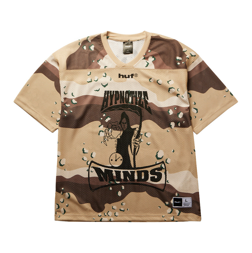 Front flat lay view of the Huf X Three 6 Mafia Football Jersey, featuring an oversized athletic mesh short-sleeve silhouette covered in a tan and brown desert six-color chocolate-chip camouflage pattern, ribbed V-neck collar, bold black lowercase "huf®" chest print, a large center graphic of the Hypnotize Minds grim reaper clutching an hourglass, arched banner typography, and a woven collaborative athletic locker tag at the bottom hem.