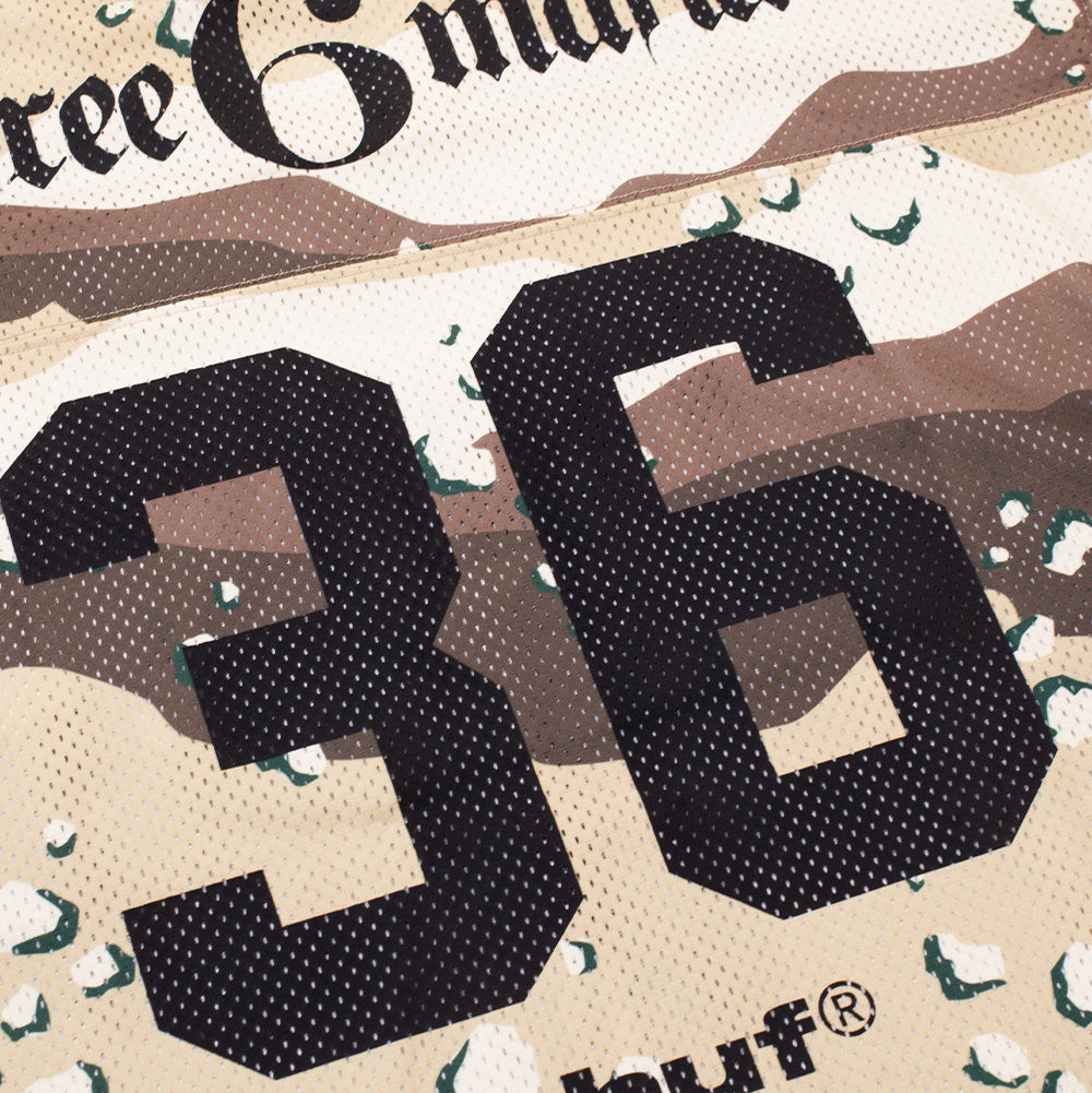 Close-up angled shot of the rear graphic on the Huf X Three 6 Mafia Football Jersey, detailing the bold black screen-printed varsity number "36" and parts of the "three 6 mafia" and "huf®" logos set against the chocolate-chip desert camouflage open-hole mesh fabric.