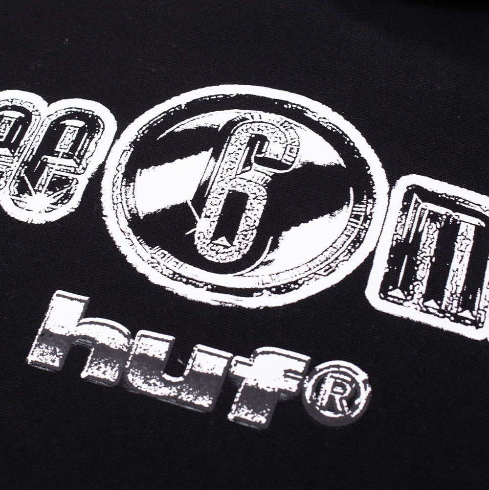 Macro studio close-up of the front chest graphic on the Huf X Three 6 Mafia Heavyweight Hoodie, highlighting the textured white screen print with subtle halftone detailing on the circular "6" badge, bold block typography of "three 6 mafia", and the blocky lowercase "huf®" trademark logo against deep black fleece fabric.