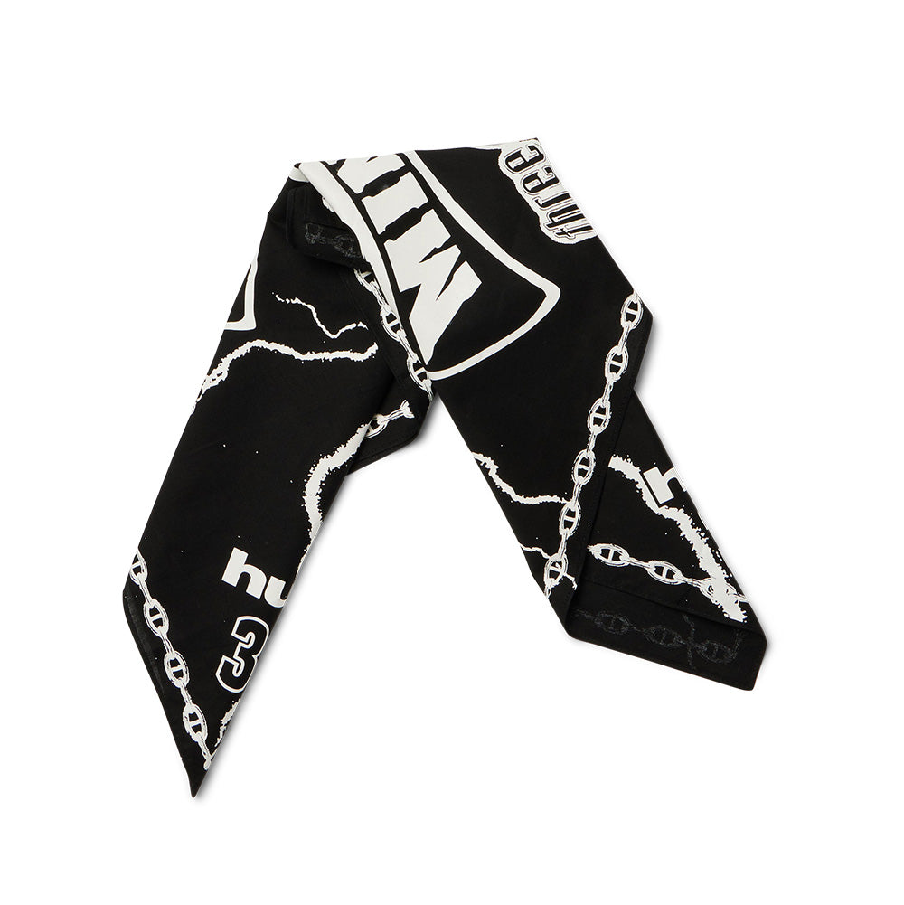 Folded flat view of the Huf X Three 6 Mafia Hypnotize Minds Bandana arranged in a diagonal neckerchief style, highlighting the crisp white screen-printed link chains along the hem, visible "three 6 mafia" and "huf®" branding, jagged lightning bolt patterns, and bold "MINDS" lettering on soft black lightweight cotton fabric.