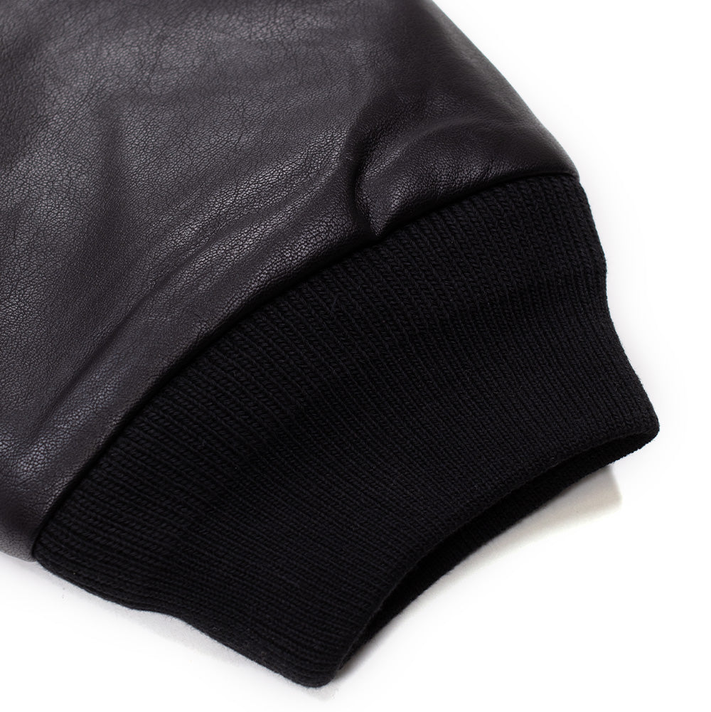 Detailed close-up of the sleeve cuff on the Huf X Three 6 Mafia jacket, showing the clean transition from the textured black faux leather to the stretchy, dense black ribbed knit fabric.