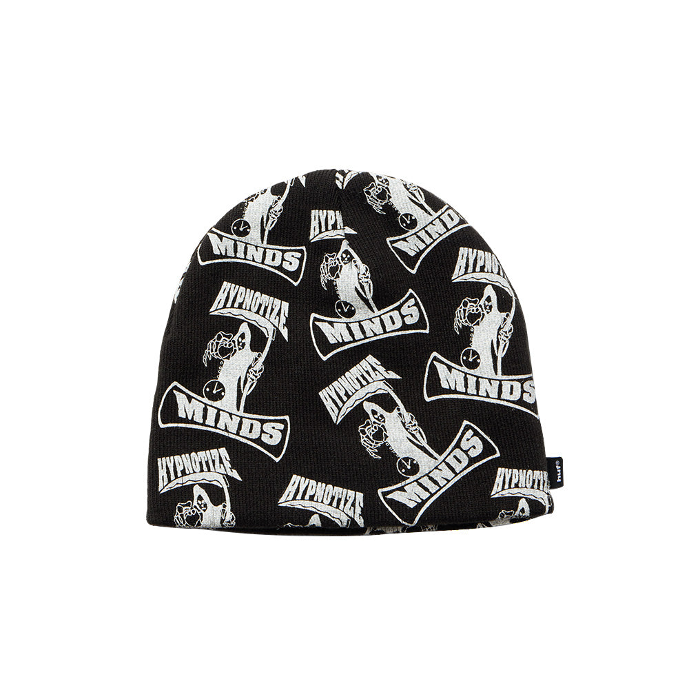 Front studio view of the black Huf X Three 6 Mafia Skull Beanie, showcasing an unrolled close-fitting knit skull cap silhouette covered in a high-contrast white jacquard repeat pattern of the Hypnotize Minds record label grim reaper holding an hourglass clock, framed by arched "HYPNOTIZE" and "MINDS" text banners, finished with a small black woven HUF brand flag label sewn onto the edge.