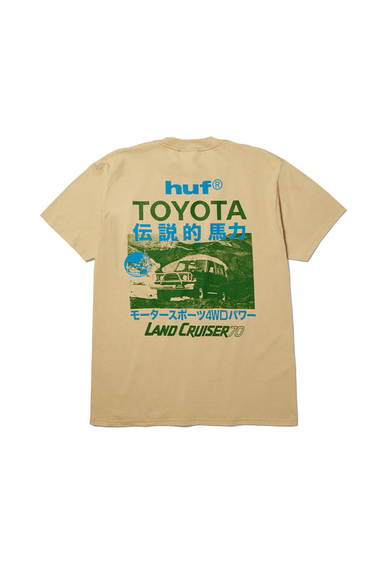 Back flat lay view of the sand beige Huf X Toyota Land Cruiser 70 SS T-Shirt made from 200g cotton, showcasing an oversized vintage off-road poster graphic on the back featuring a green-toned photograph of a classic Toyota Land Cruiser 70 climbing rocky terrain, accompanied by bold blue "huf®", dark green "TOYOTA", and bright blue Japanese Kanji characters.