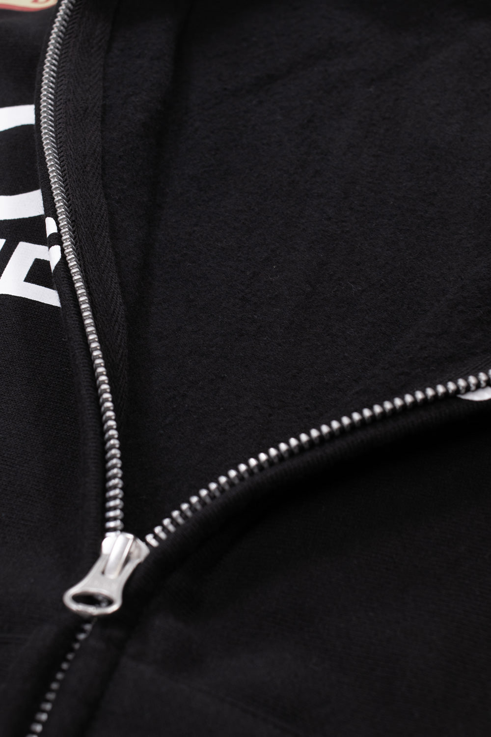 Macro close-up perspective of the front zipper closure on the Huf X Toyota Land Cruiser Heavyweight FZ Hoodie, showcasing the silver metallic YKK zipper pull and teeth, neatly stitched placket edge, and the plush brushed interior texture of the 420-gram heavyweight black cotton fleece.