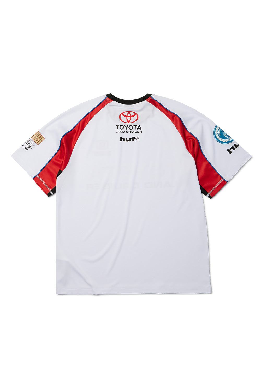 Back flat lay view of the white Huf X Toyota Land Cruiser Rally Jersey, displaying the dynamic red raglan shoulder seams accented by blue piping, contrasting black underarm inserts, and upper back neck graphics featuring the red Toyota logo, "LAND CRUISER" text, and the black lowercase "huf®" wordmark.