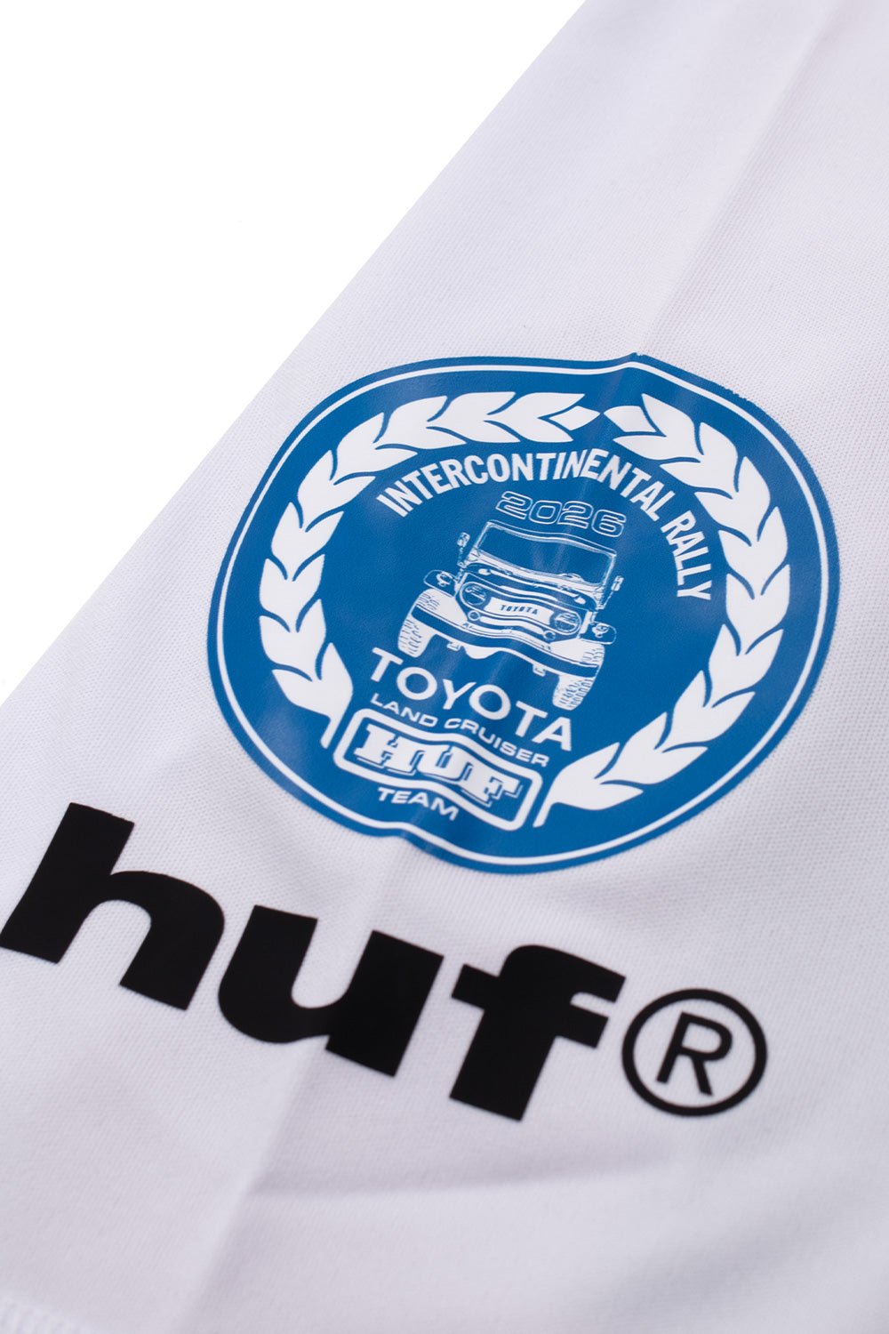 Detailed close-up shot of the left sleeve decal on the Huf X Toyota Land Cruiser Rally Jersey, displaying a circular blue-and-white laurel wreath emblem reading "INTERCONTINENTAL RALLY 2026" featuring an illustrated Toyota FJ Land Cruiser and "HUF TEAM" banner above bold black "huf®" lettering.