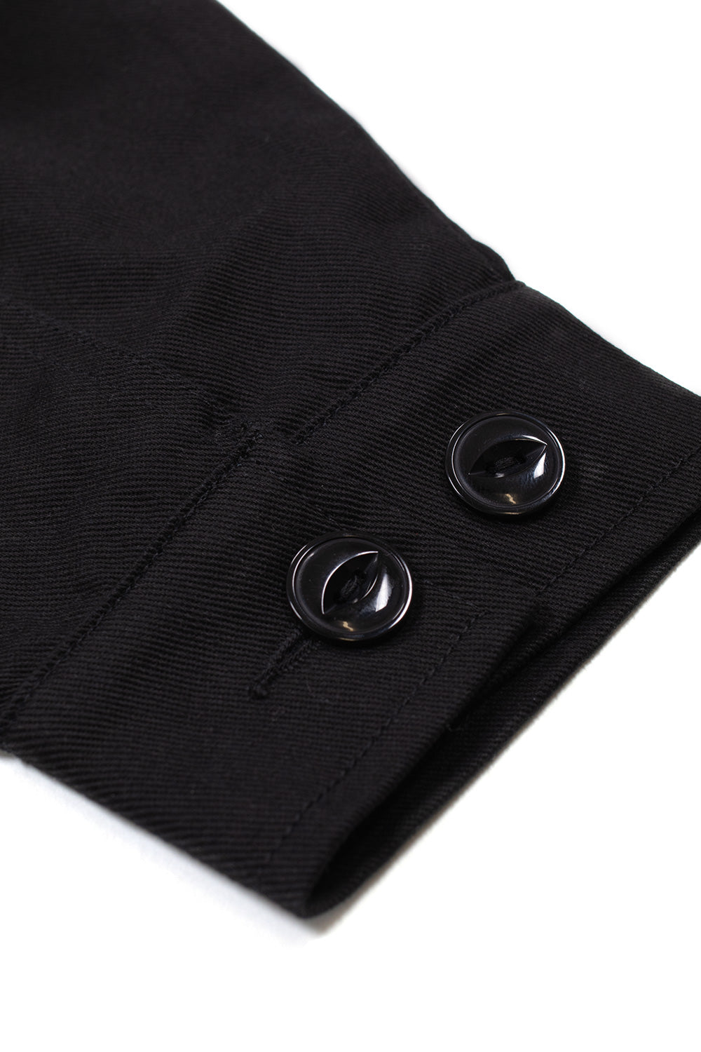 Macro studio close-up of the sleeve cuff on the Huf X Toyota Land Cruiser World Tour Jacket, showing the dual black cat-eye button adjustments, clean buttonhole stitching, and the durable woven texture of the 280-gram black cotton twill