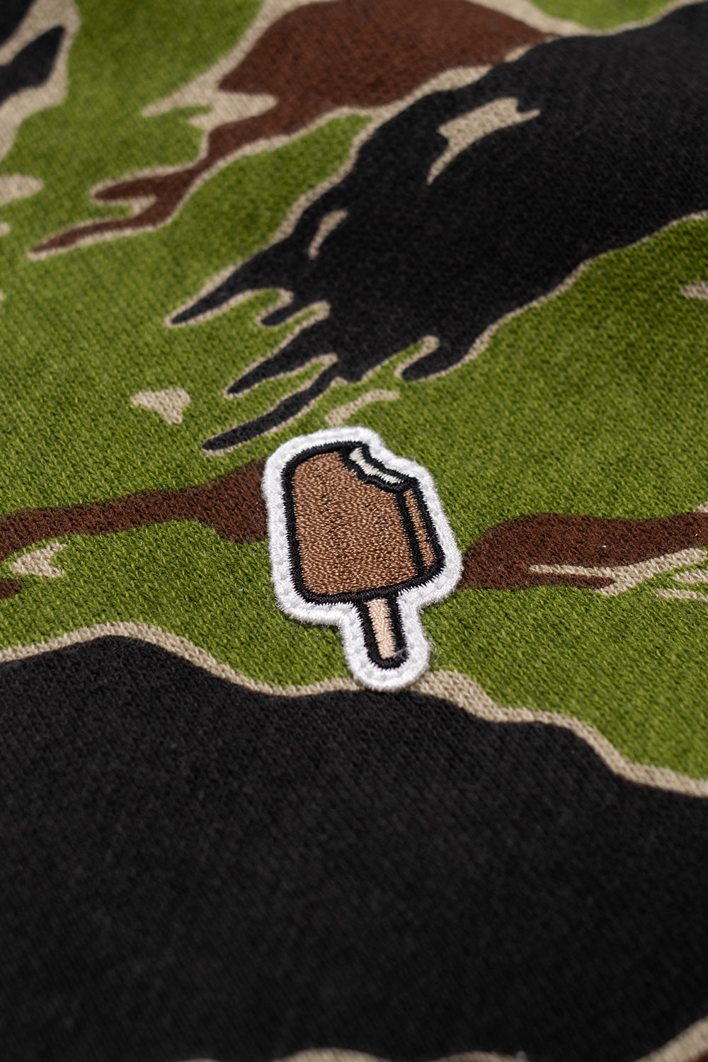 Embroidered IceCream popsicle patch detail on chest of Tiger Stripe camo full zip hoodie, showcasing signature Pharrell Williams skate-inspired branding.