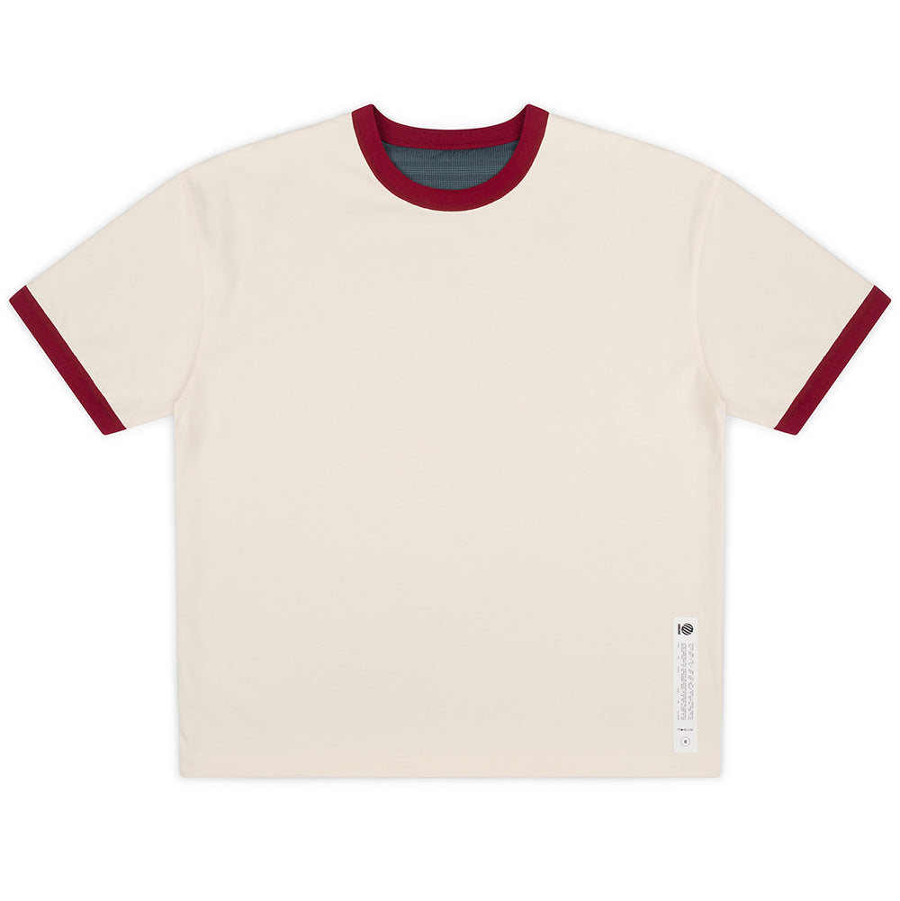 Front flat lay studio view of the Metalwood Studio Dual Face T-Shirt in Bone, showcasing a relaxed boxy cut in off-white cream cotton jersey, featuring contrast burgundy rib-knit crewneck collar and sleeve cuffs, an exposed blue grid patterned inner lining at the neck, and an exterior white vertical care instruction patch stitched above the lower left hem.