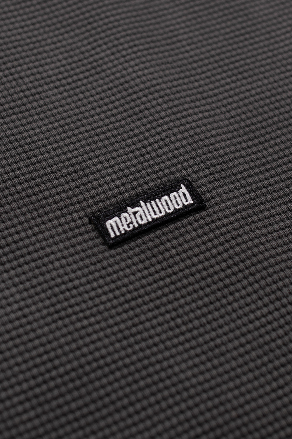 Close-up of Metalwood Studio Mini Metal Logo Thermal Shirt Tar showing textured waffle knit fabric and small stitched Metalwood logo patch on left chest.