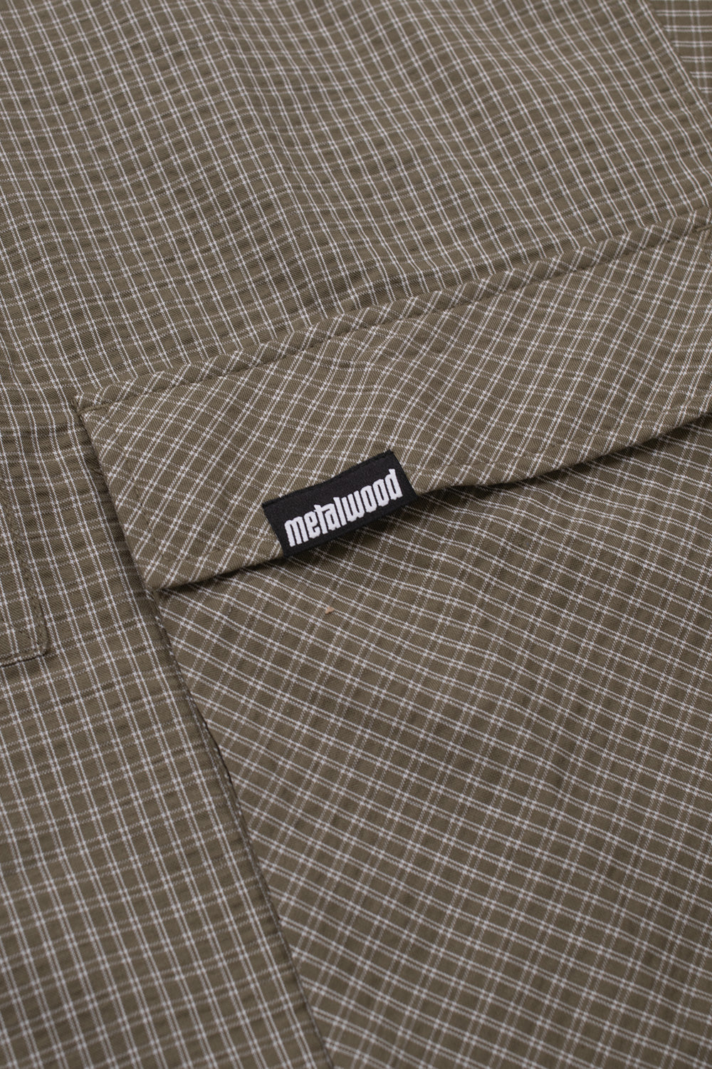 Metalwood Studio Plaid Tactical Overshirt pocket detail featuring oversized flap pocket, woven logo label and utility-inspired storage design in green plaid cotton