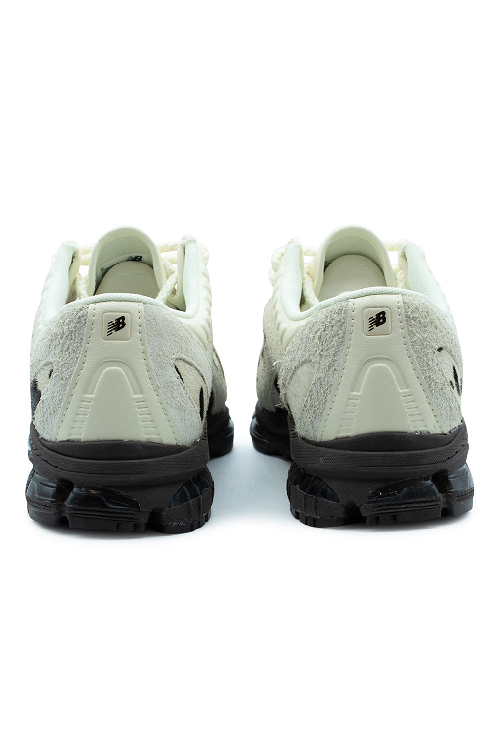 Rear perspective shot of the heels of the New Balance 1890A sneakers, displaying the brushed off-white shaggy suede heel counters, central smooth leather vertical spine overlays with embossed black "NB" logo emblems, ribbed textile collar edges, and the chunky black segmented ABZORB SBS heel unit.