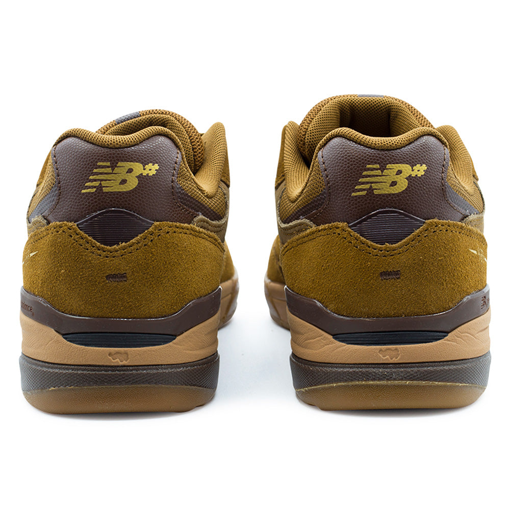 Rear studio view of the New Balance Numeric Andrew Reynolds 933 heel construction, showcasing the padded mesh ankle collars, dark pumpernickel brown leather heel tabs featuring gold embroidered NB# logos, roughout golden-brown suede heel counters, and stacked dual-density gum rubber cupsole outsoles.