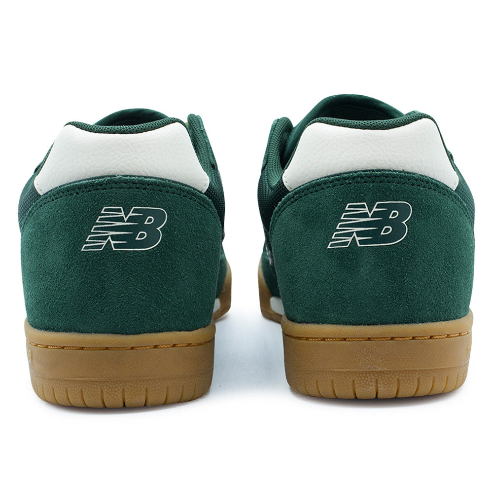 Rear studio view of the New Balance Numeric Tom Knox 600 heel design, displaying the Nordic Green suede heel counters with white embroidered Flying NB logos, contrasting smooth white leather collar tabs, padded green lining, and textured gum rubber outsoles with reinforcement stitching.