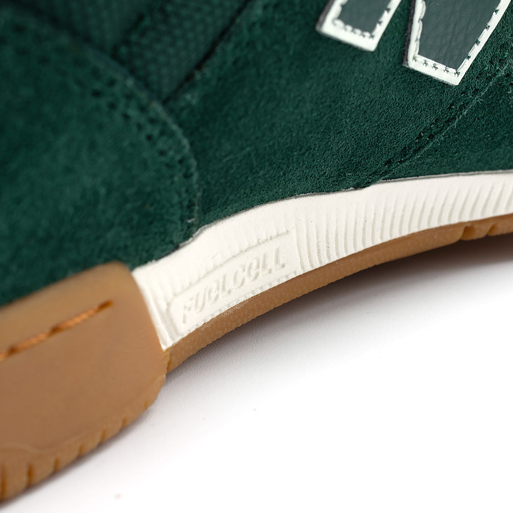 Macro studio close-up of the midsole on the New Balance Numeric Tom Knox 600, focusing on the white technical FuelCell foam cushioning wedge debossed with "FUELCELL" branding, set between the rich green suede upper and stitched gum rubber cupsole.