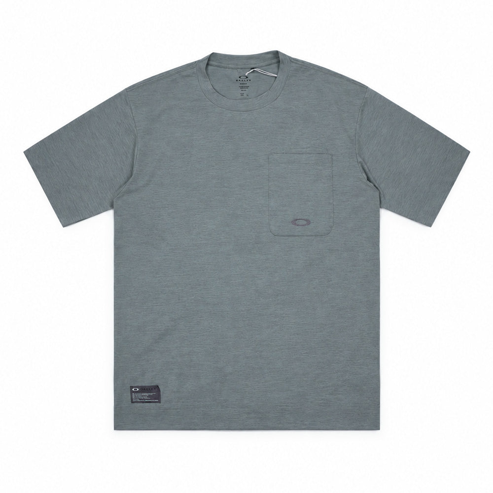 Front flat lay studio view of the Oakley FGL Scratch Short Sleeve Tee 6.7 in Acrid Green, showcasing a heathered sage-green technical jersey performance t-shirt, ribbed crewneck collar, short sleeves, a structured utility patch pocket on the left chest with an integrated tool compartment and tonal embroidered scratch logo, and an authentic dark grey Oakley FGL military-spec woven patch on the lower right hem.