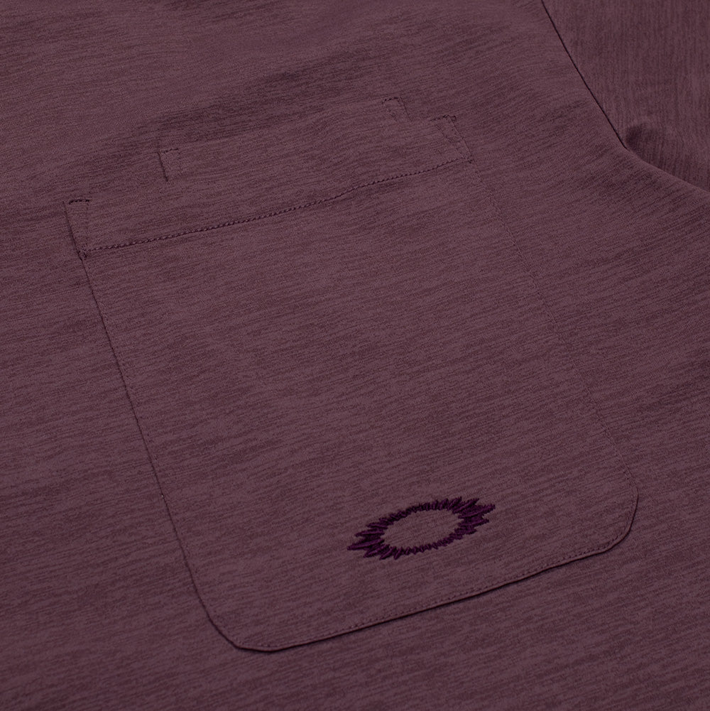 Macro studio view of the left chest pocket on the Oakley FGL Scratch SS Tee, displaying the double-stitched top hem with integrated tool compartment and dense tonal burgundy thread embroidery outlining the jagged, scratch-style Oakley Ellipse icon at the bottom of the pocket.