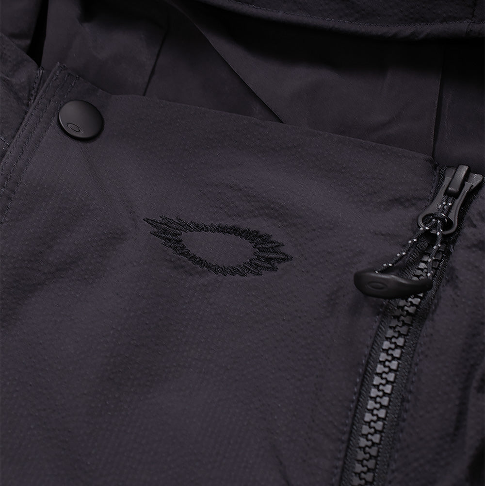Detailed macro perspective of the high-collar closure on the Oakley FGL Stroke Anorak in Phantom, highlighting the storm placket with matte black snap fastener, asymmetrical zip closure with textured ring pull cord, and the tonal black embroidered jagged scratch outline of the Oakley Ellipse logo on the neck gusset.