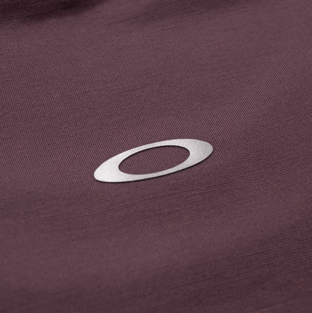 Extreme macro close-up of the back neck logo on the Oakley FGL Union SS Tee, displaying the heat-transferred reflective silver Oakley Ellipse icon cleanly bonded onto the fine-textured rouge purple technical fabric.