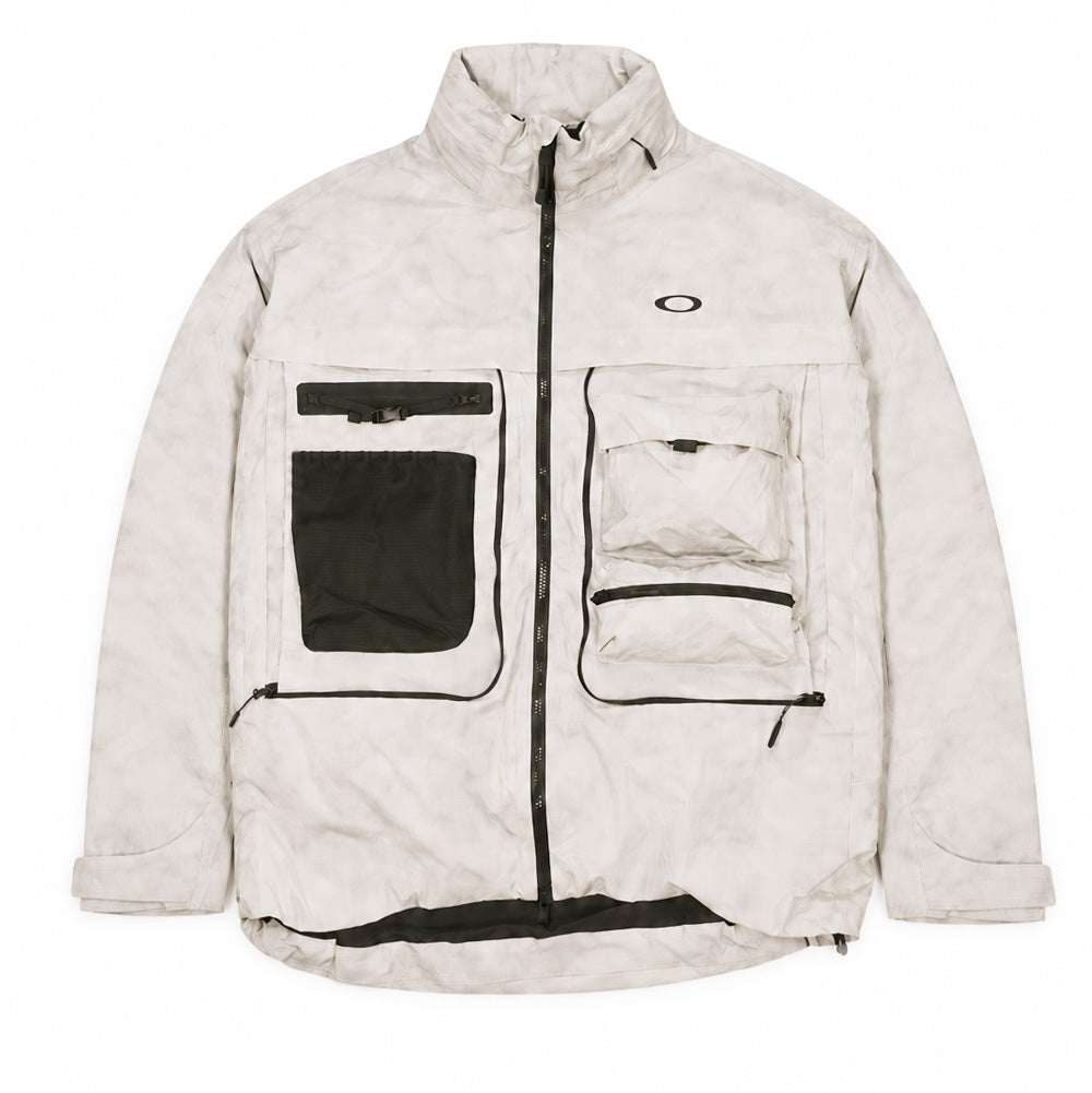 Front flat lay view of the Oakley Mthod Glow Shell Jacket in Reflective Camo Mist showing the full technical pocket configuration, featuring high-contrast black zippers, black mesh stash pouch on the right chest, dual stacked flap and zip utility pockets on the left chest, high collar, and center two-way zip closure.