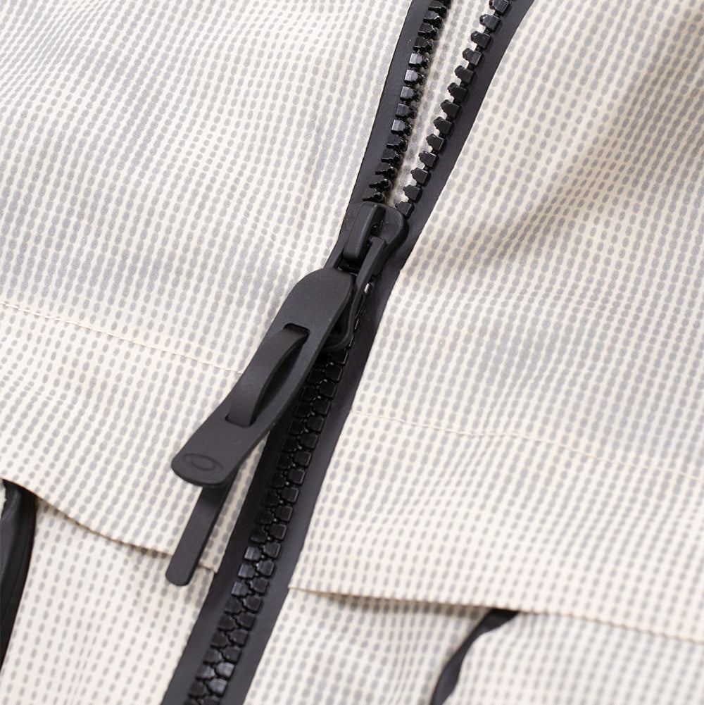 Macro studio close-up of the front zipper on the Oakley Mthod Glow Shell Jacket, detailing the chunky black two-way Vislon AquaGuard teeth, molded ergonomic zipper pull tab debossed with the Oakley Ellipse logo, and the fine-textured dot-grid weave of the technical shell fabric.
