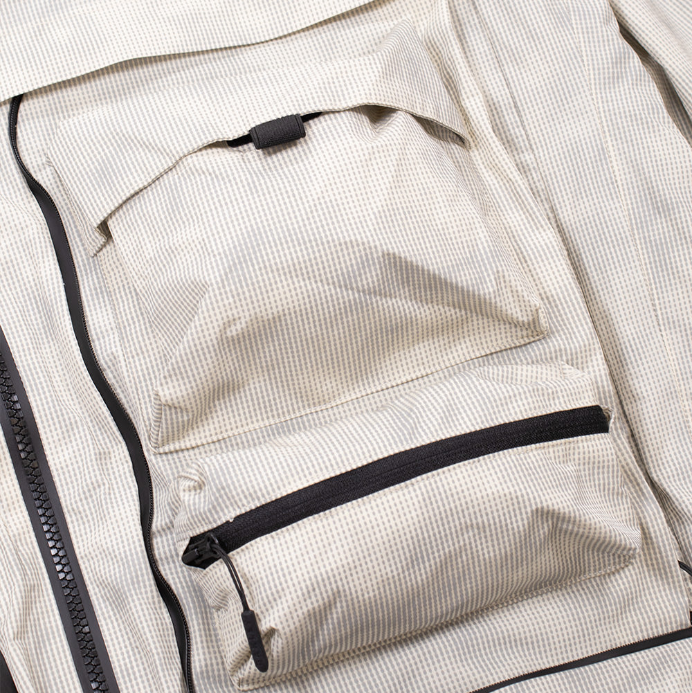 Macro studio view of the left chest modular utility compartment on the Oakley Mthod Glow Shell Jacket, showcasing the 3D bellowed cargo pocket with pull tab closure, horizontal taped zip pocket below, and black weatherproof perimeter zips.