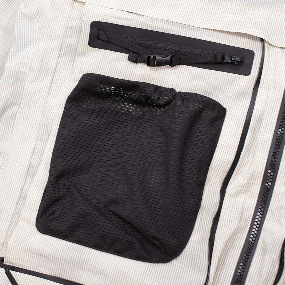 Detailed close-up shot of the right chest utility pocket on the Oakley Mthod Glow Shell Jacket, highlighting the breathable black mesh pouch with an elasticated top rim, positioned beneath a waterproof zippered pocket with black webbing strap and miniature buckle.