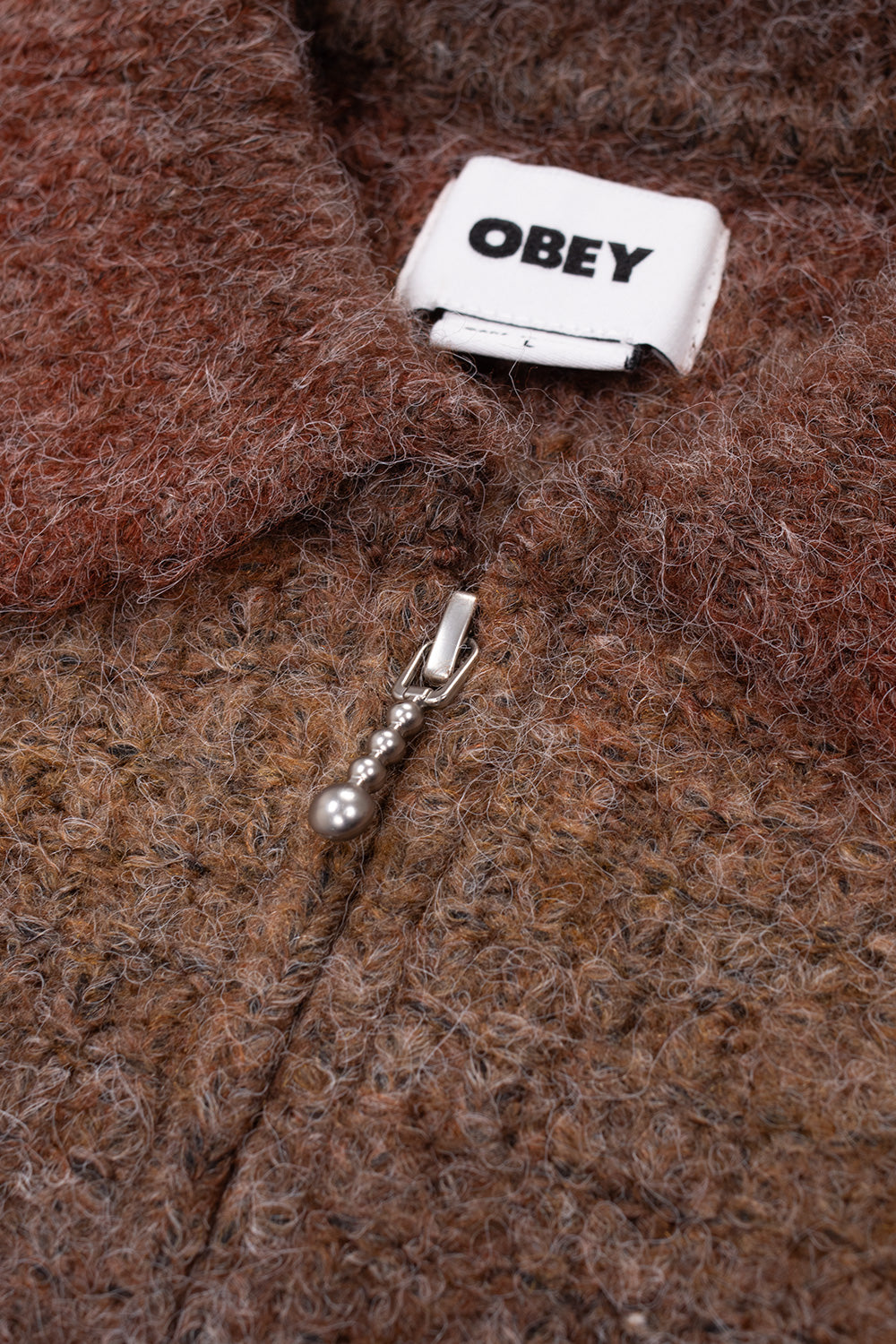 Close-up detail shot of the neckline and zipper closure on the Obey Anton Cardigan, displaying the tactile hairy yarn texture, white interior Obey neck tag, and antique silver metal zip pull crafted from stacked metallic beads.