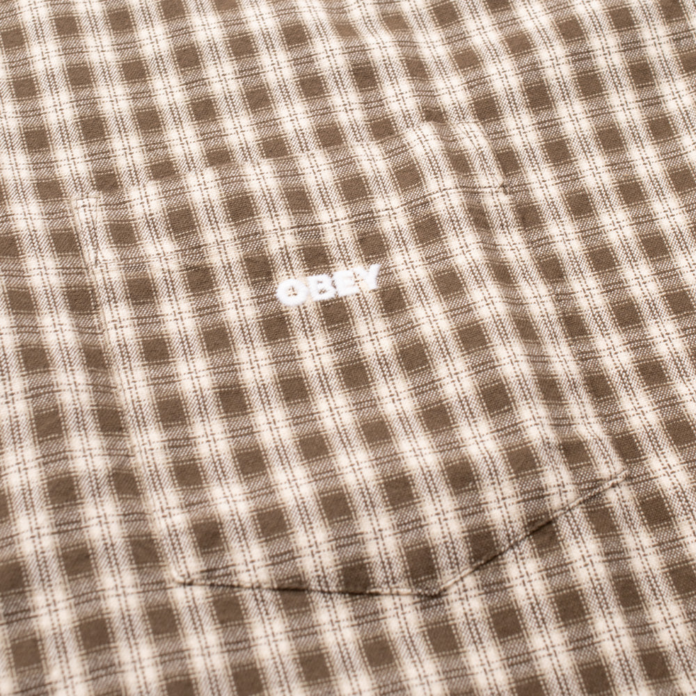 Detailed close-up shot of the left chest pocket on the Obey Bigwig Axel Woven Shirt, focusing on the seamless plaid pattern alignment and the clean white satin-stitched "OBEY" logo embroidery centered on the pocket face.