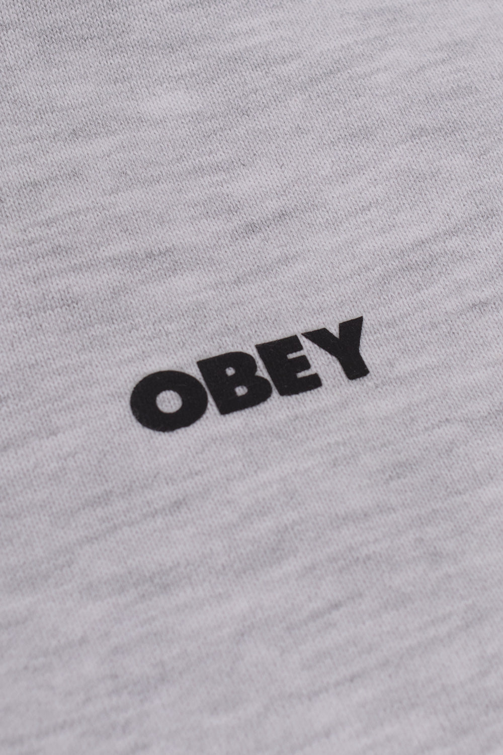 Macro detail view of the solid black Obey bold text logo printed across the fine ash grey cotton-poly knit fleece on the front chest of the hooded sweatshirt.