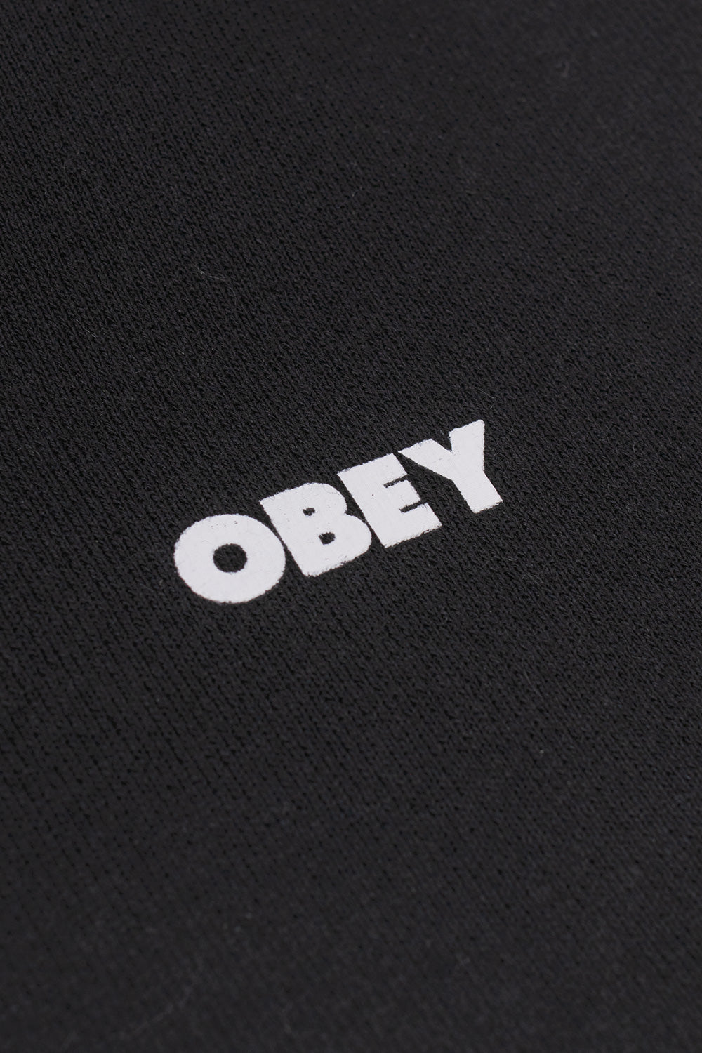 Macro detail view of the solid white Obey bold logo text printed across the textured black heavy cotton-blend fleece on the front chest of the hoodie.