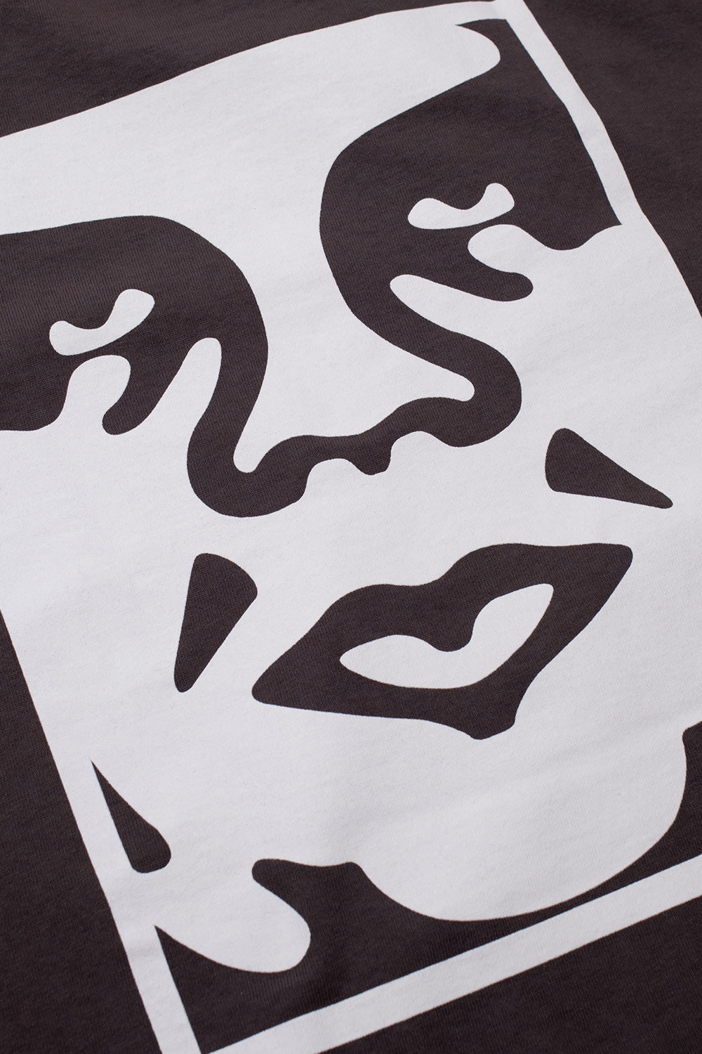 Detailed close-up shot of the high-contrast white Shepard Fairey Giant Icon face screen print on the washed black heavy cotton back panel of the Obey Bold Icon Face tee.