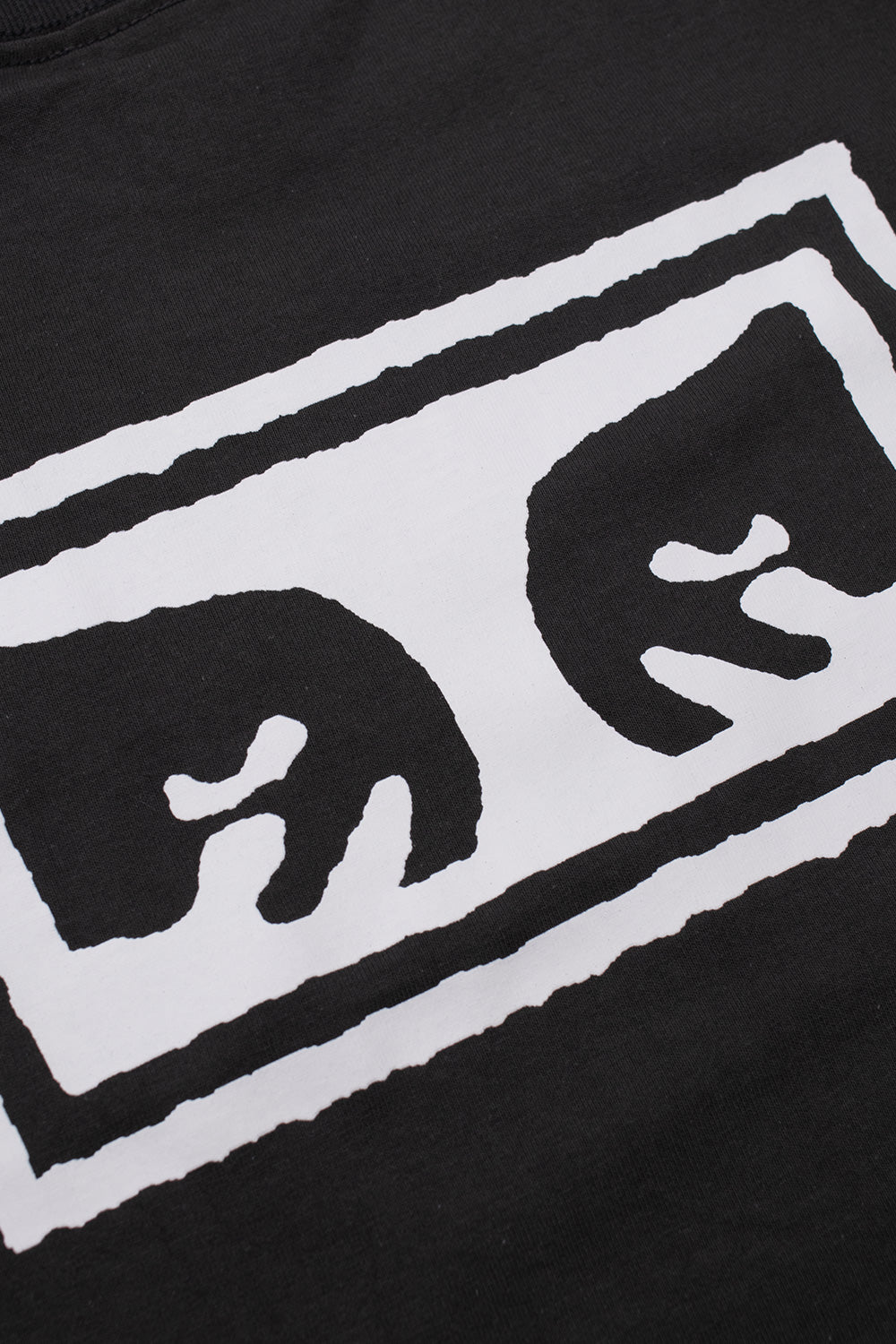 Detailed close-up shot of the white textured Giant Eyes screen print with rough distressed border edges on the washed vintage black heavy cotton back panel of the Obey Eyes 3 tee.