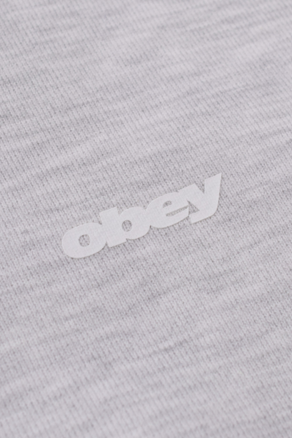 Macro detail view of the minimalist white Obey bold text logo printed on the fine heather ash grey cotton-poly fleece fabric on the front chest of the hooded sweatshirt.