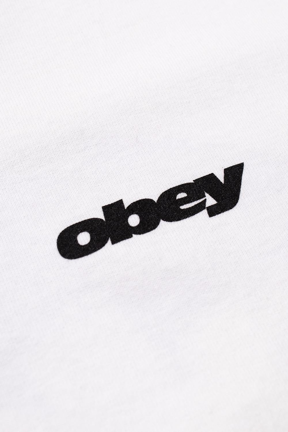 Macro detail view of the solid black Obey bold font logo printed across the fine white 100% heavyweight cotton jersey fabric on the front chest.