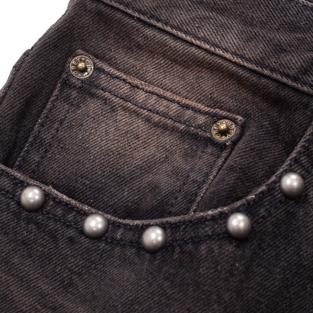 Detailed close-up shot of the front right pocket on the Obey Studded Boxcar Denim, focusing on the nested coin pocket secured by engraved brass OBEY rivets and the curving line of antique silver dome studs following the reinforced stitch line of the pocket scoop.
