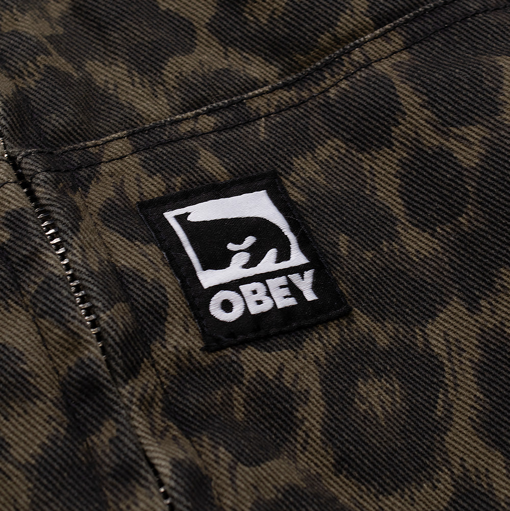 Detailed close-up shot of the front pocket branding on the Obey Studded Zip Up Jacket, showing the square black woven label featuring the white Obey Icon Eyes graphic and bold "OBEY" block typography, stitched securely onto the dark leopard printed fabric.