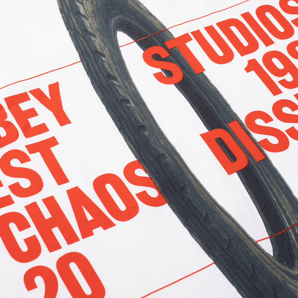 Angled macro studio close-up of the front screen print on the Obey Studios Chaos Dissent Heavyweight T-Shirt, highlighting the textured black-and-grey tread details of the painted tire graphic beneath the vibrant red block lettering on heavy white cotton jersey fabric.